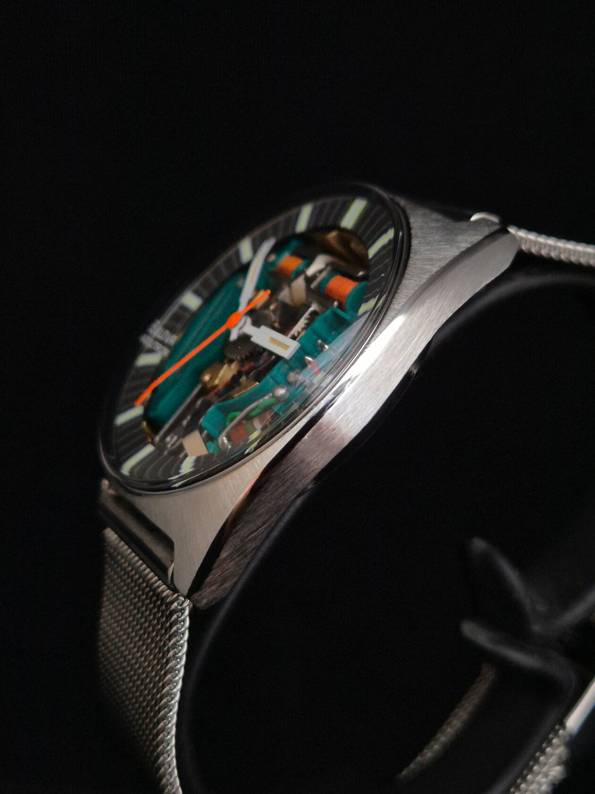 Close-up of a silver wristwatch with a translucent dial and green circuit-like details on a dark background