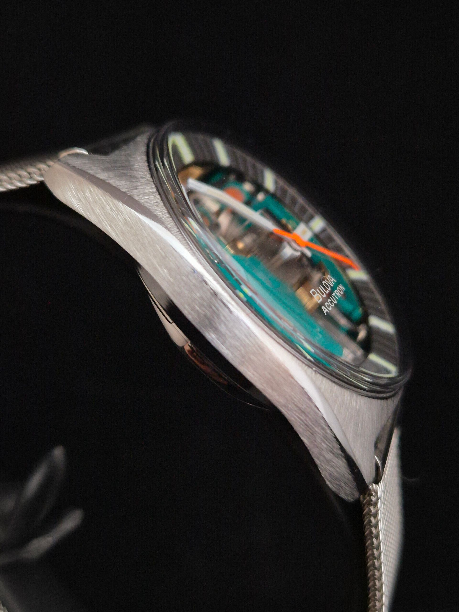 Close-up of a silver wristwatch with a visible teal and orange mechanical interior on a black background
