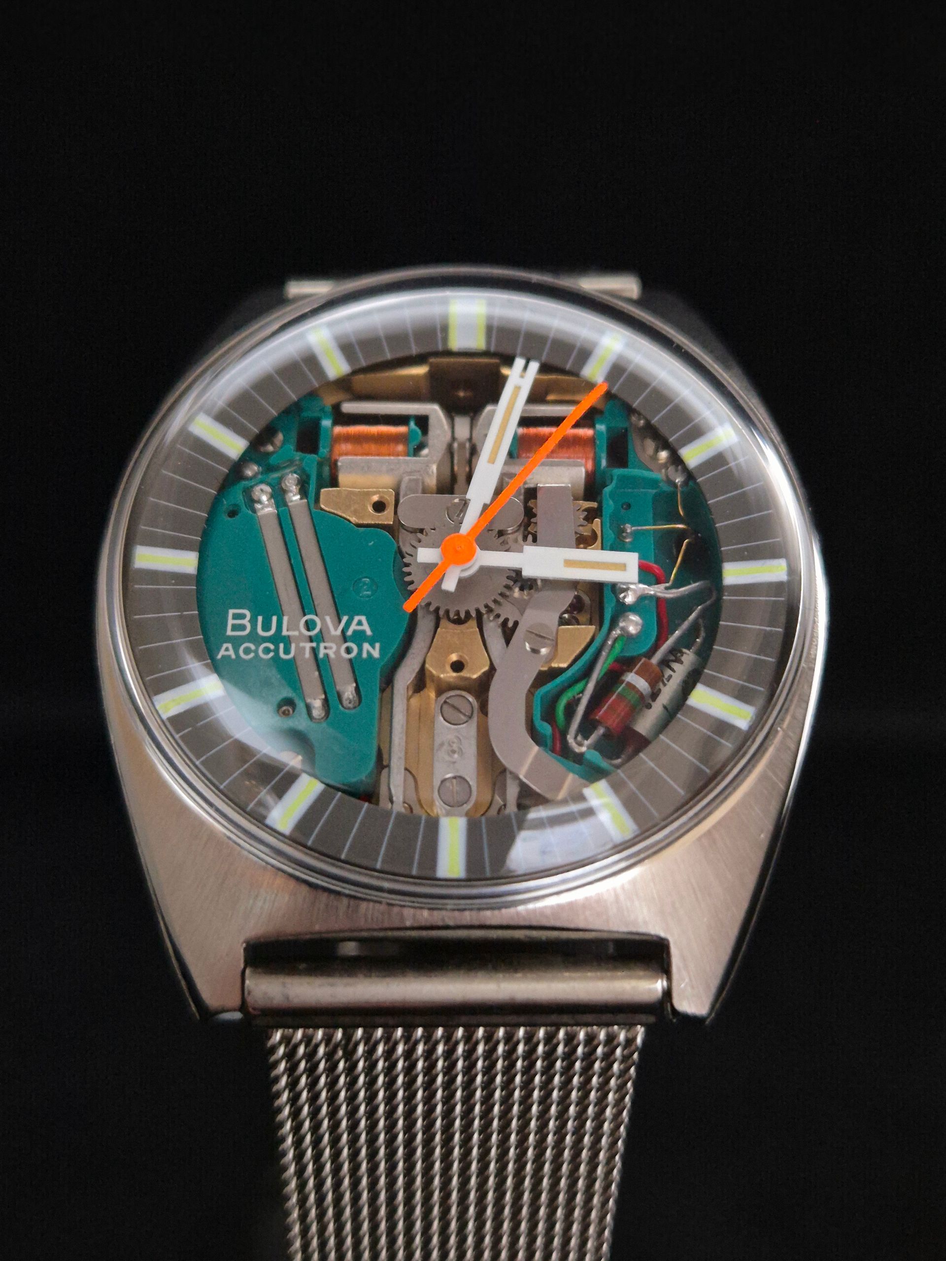 Bvlgari wristwatch with transparent dial, orange hands, and metal mesh band