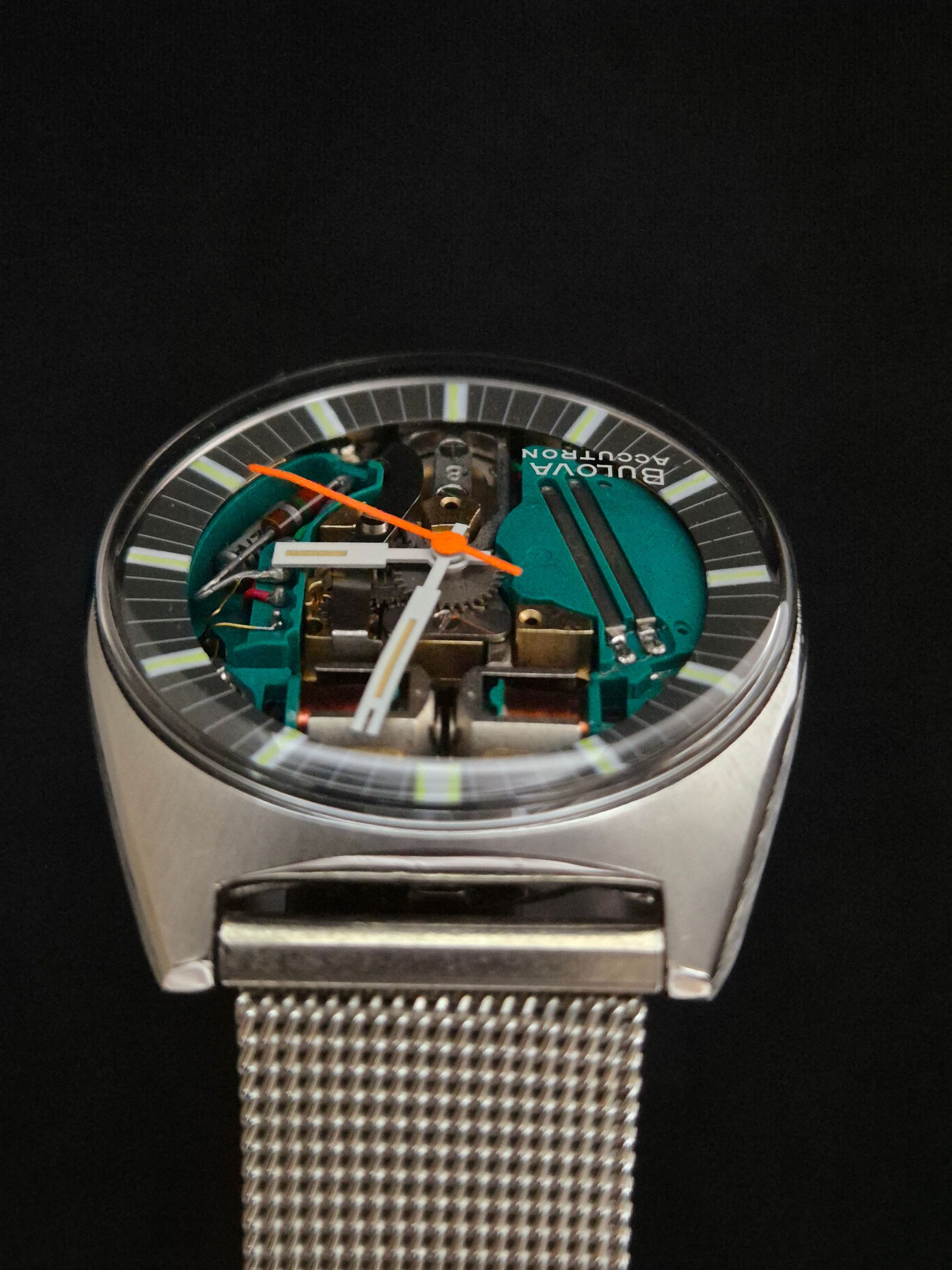 Modern wristwatch with transparent skeleton dial, orange hands, and silver mesh band