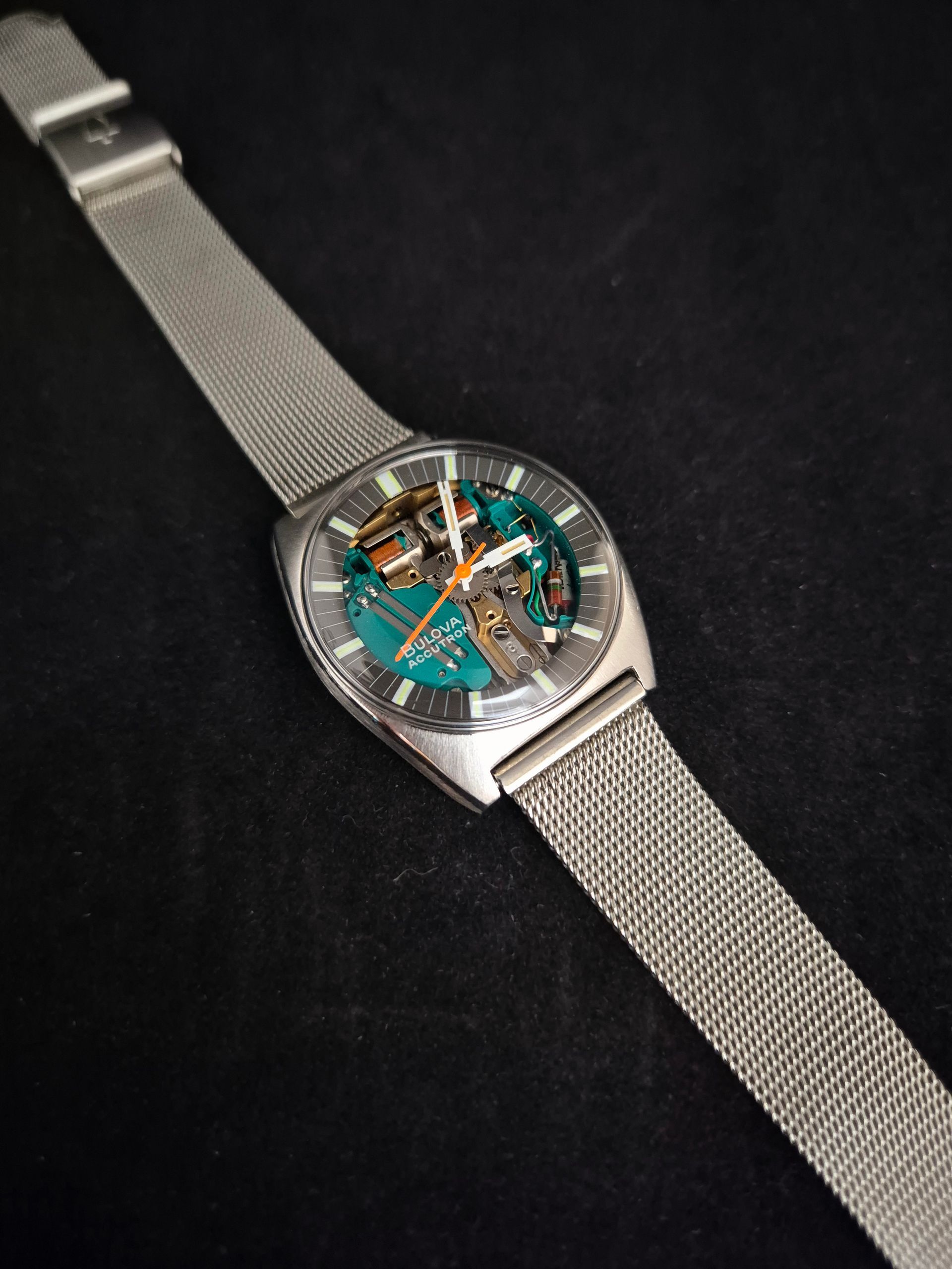 Silver wristwatch with turquoise dial and metal mesh band on a black background