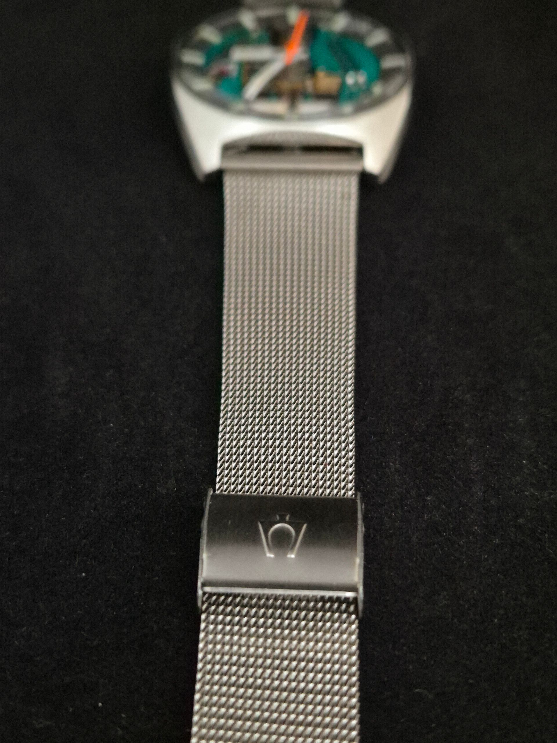 Silver mesh wristwatch with a turquoise and orange dial on a black background