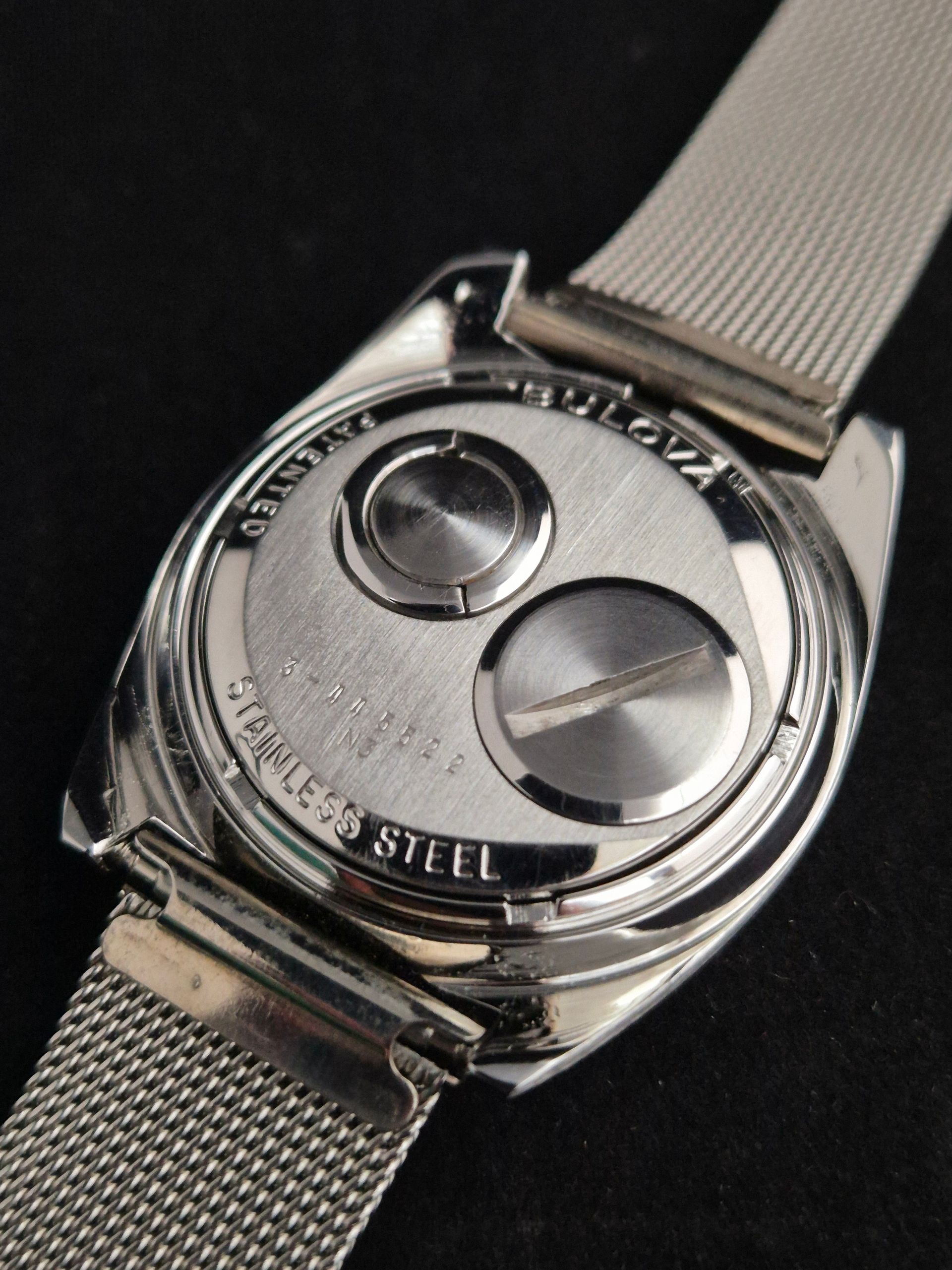 Close-up of a stainless steel watch back and mesh band on a dark background