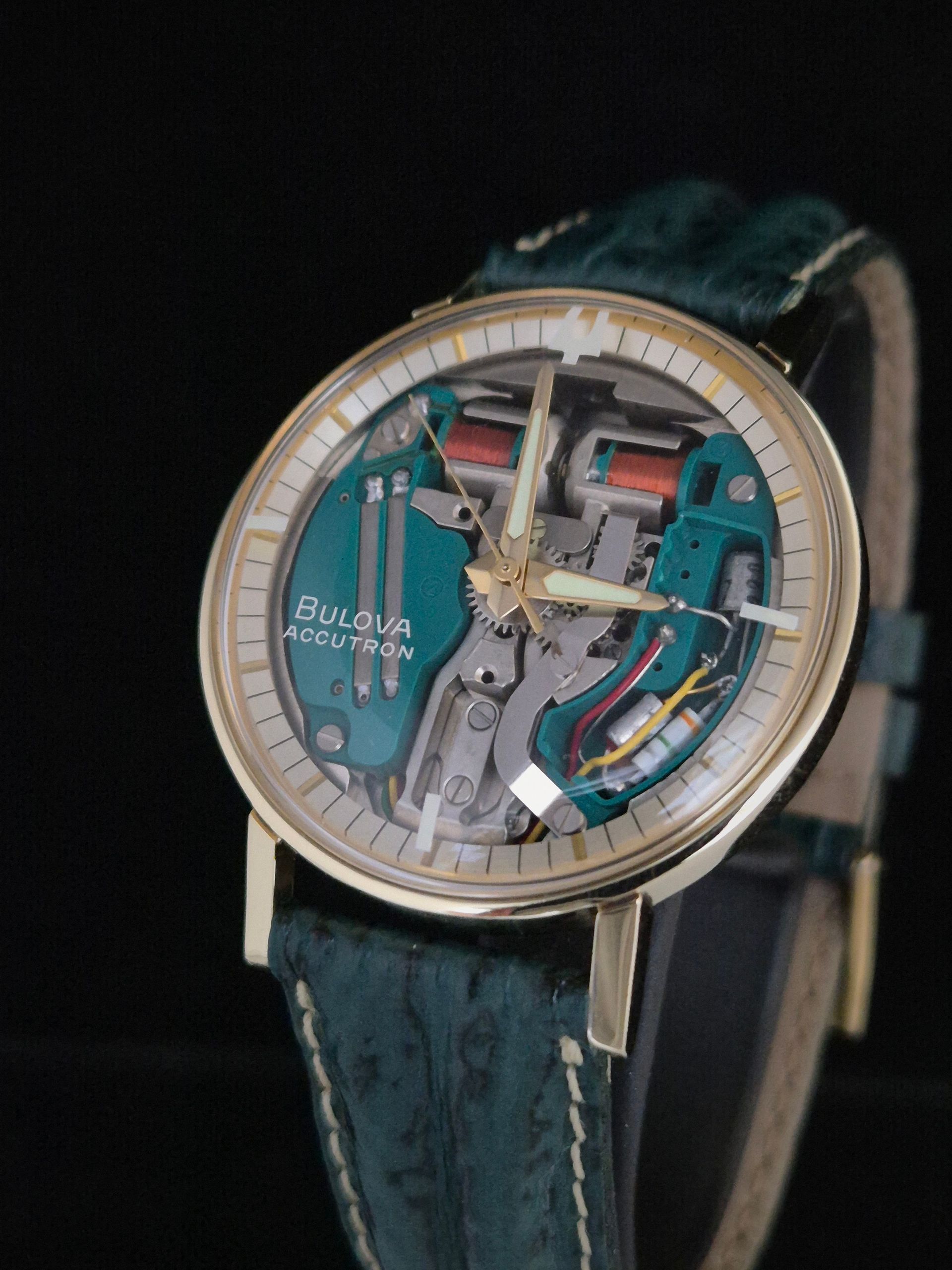 Bulova skeleton wristwatch with teal dial and gold bezel on a black strap