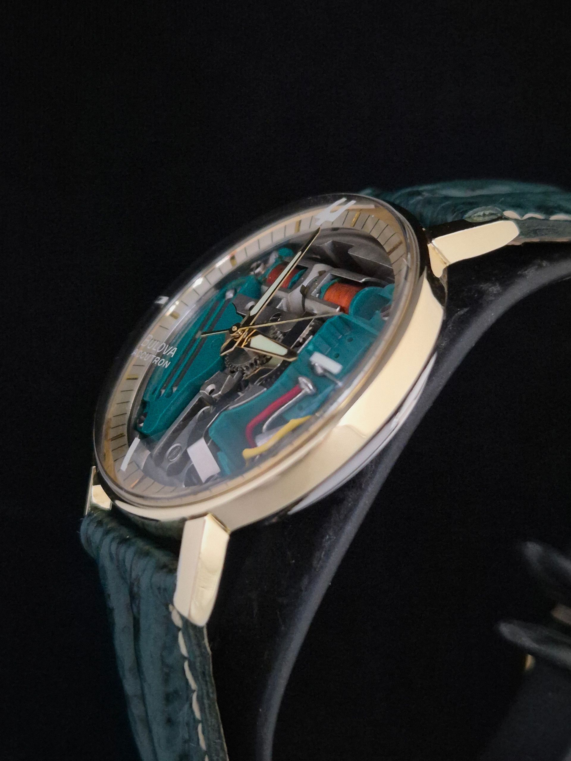 Luxury wristwatch with a teal skeletal dial, gold case, and black leather strap on a dark background