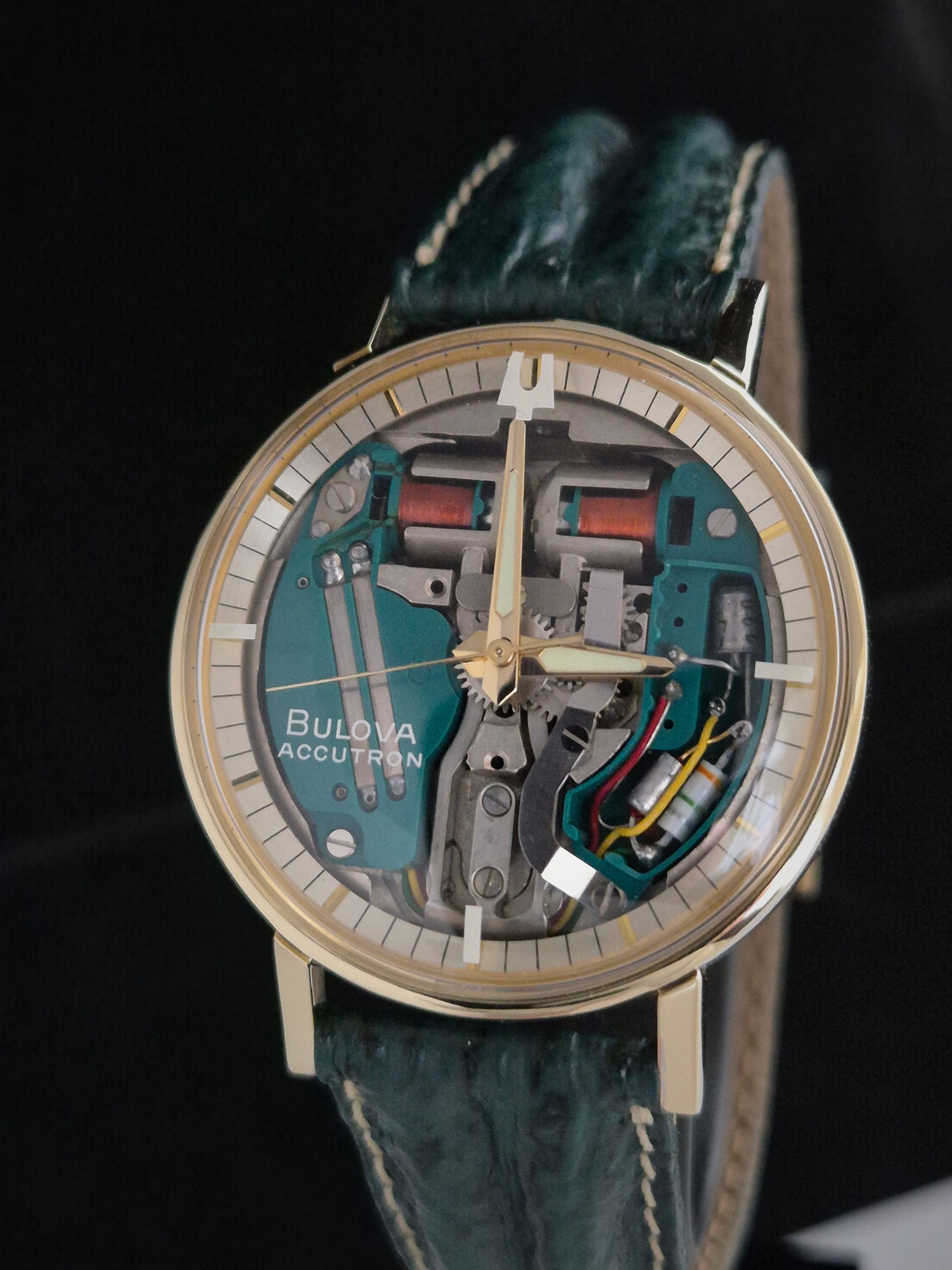 Skeleton wristwatch with exposed movement, beige bezel, and teal strap on a dark background