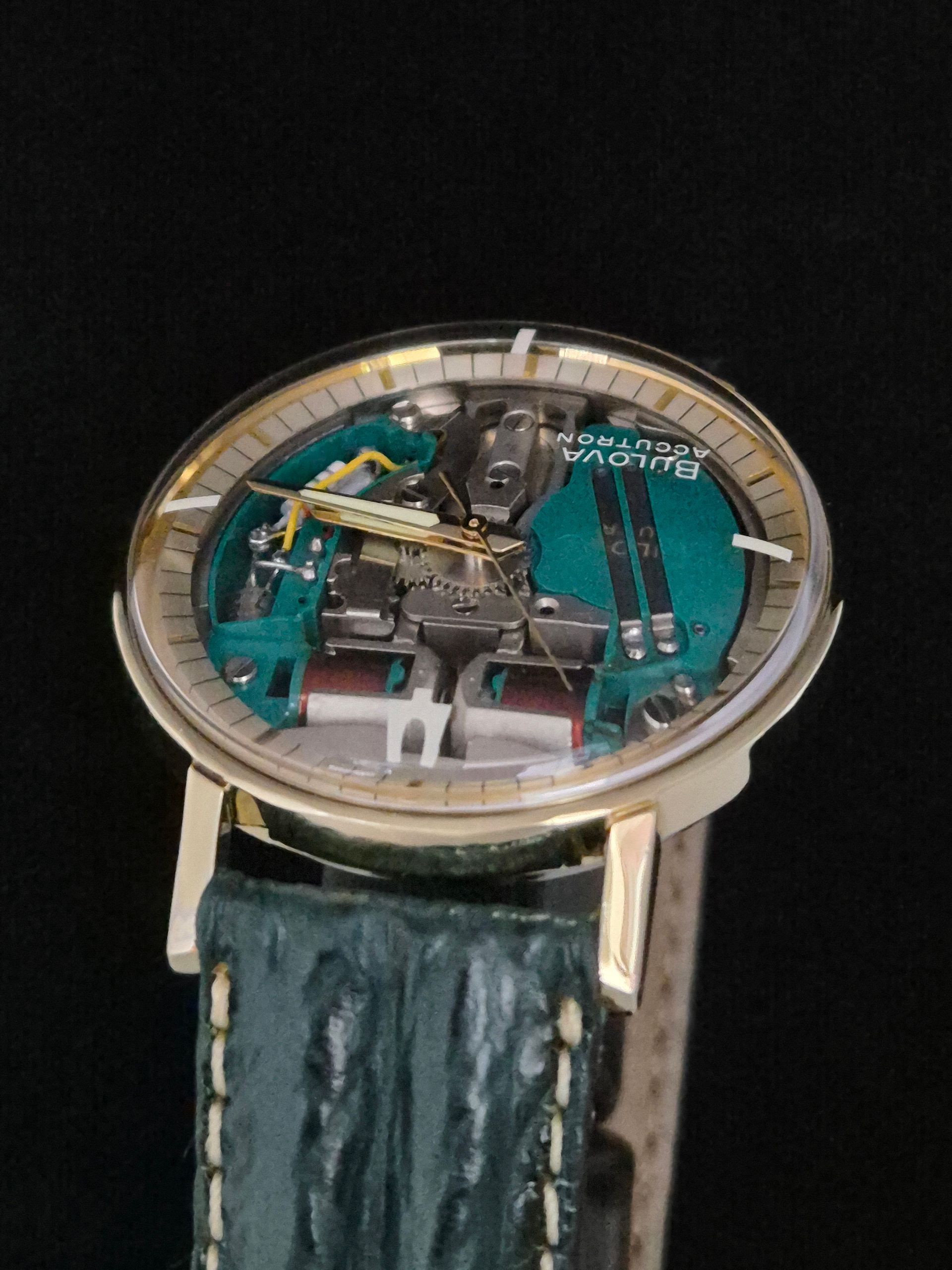 Close-up of a wristwatch with a visible skeleton mechanism and teal face on a dark strap
