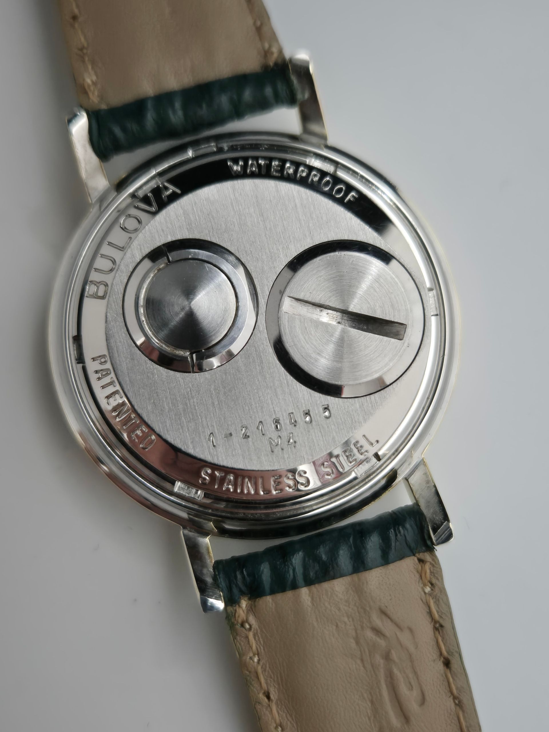 Close-up of a silver Bulova waterproof watch back on a tan strap with green tape.