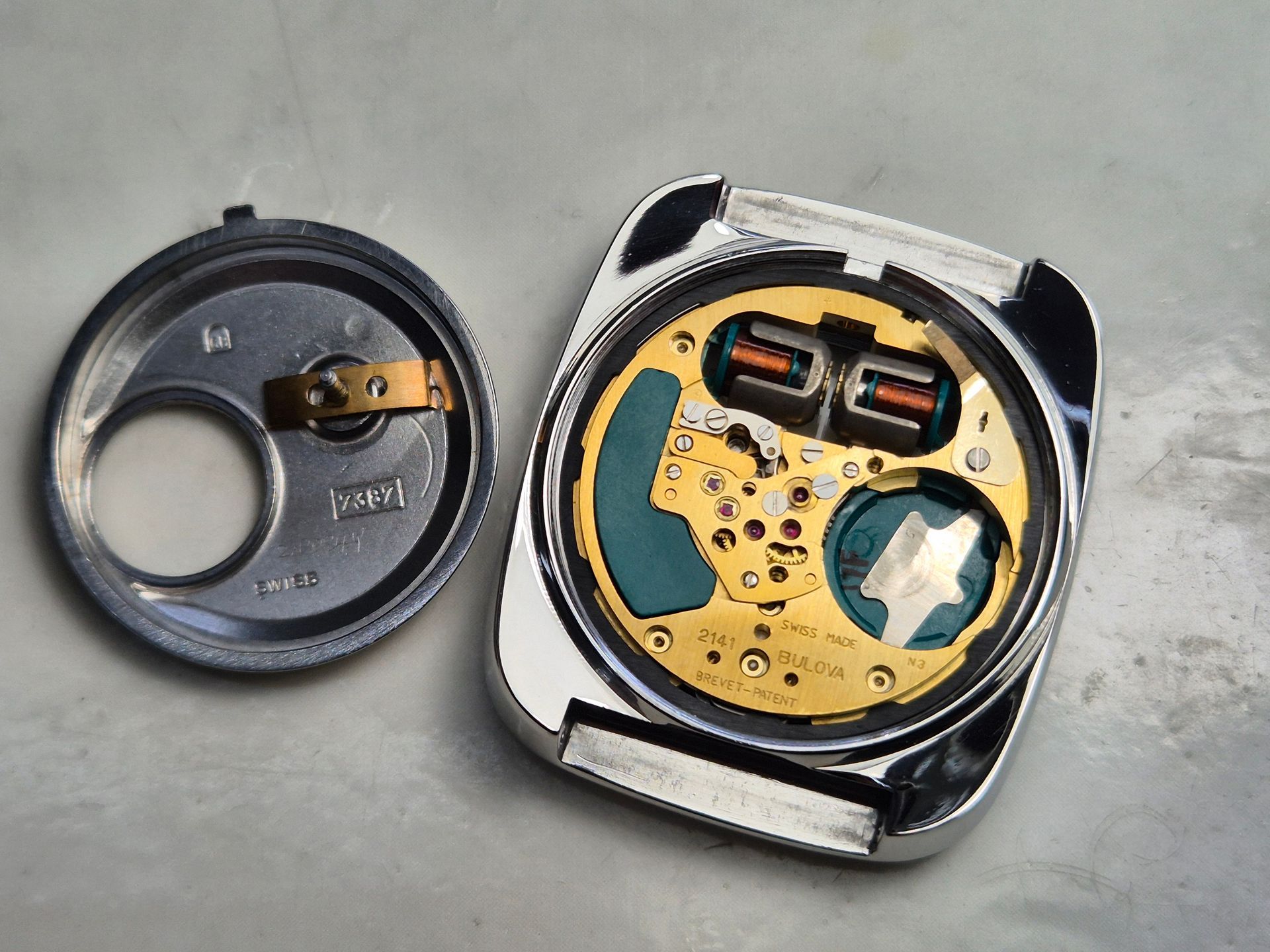 Opened wristwatch showing inner battery and movement beside its removed back cover