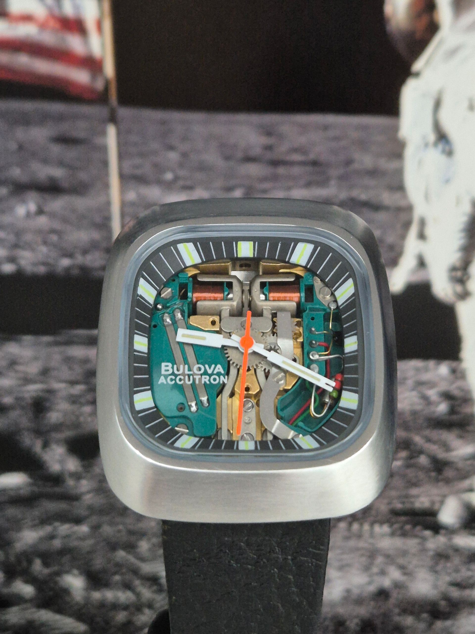 Bulova Accutron square watch with silver case, colorful skeleton dial, and black strap on display stand