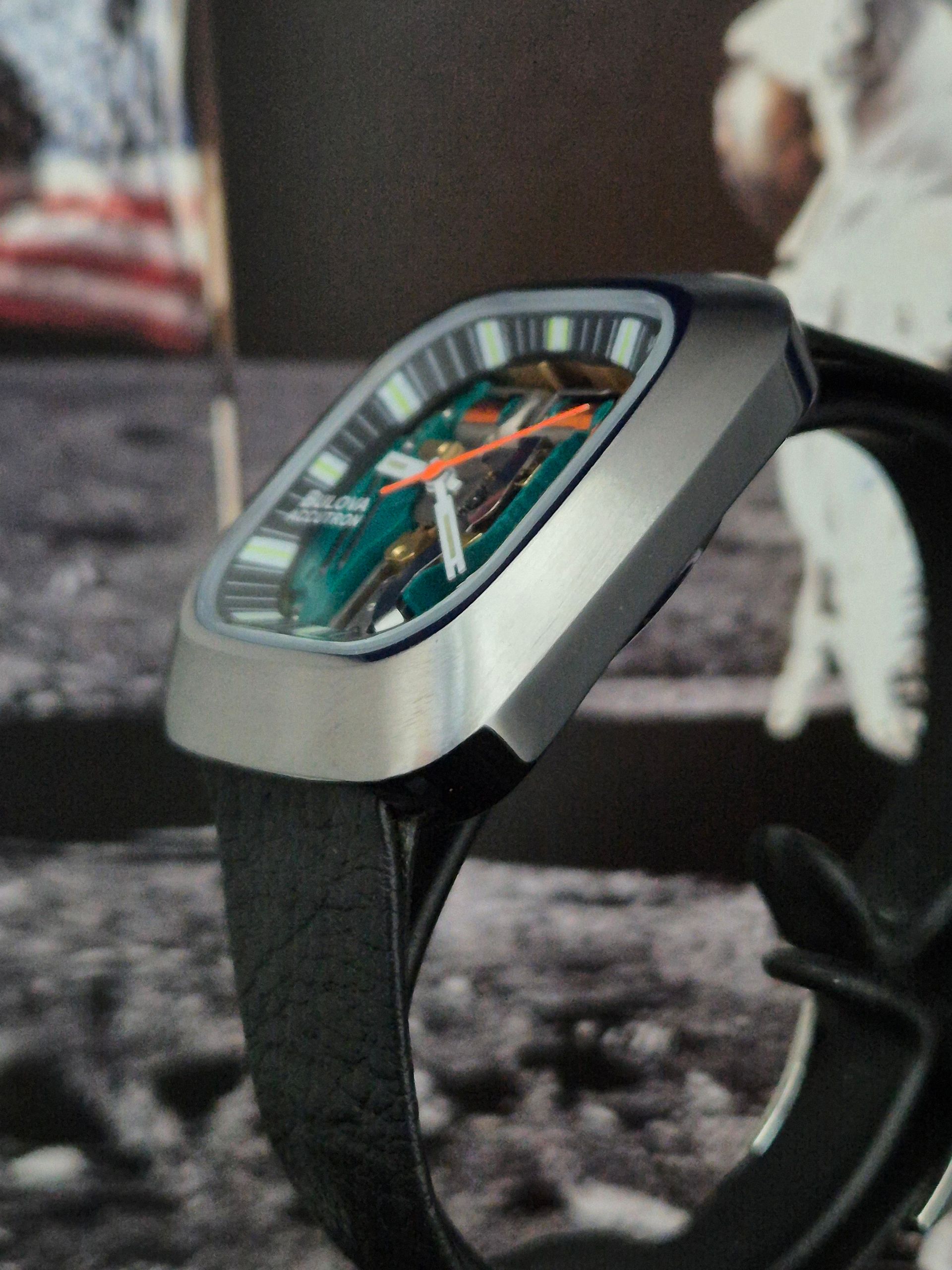 Black smartwatch with a green dial and black band on a blurred outdoor surface