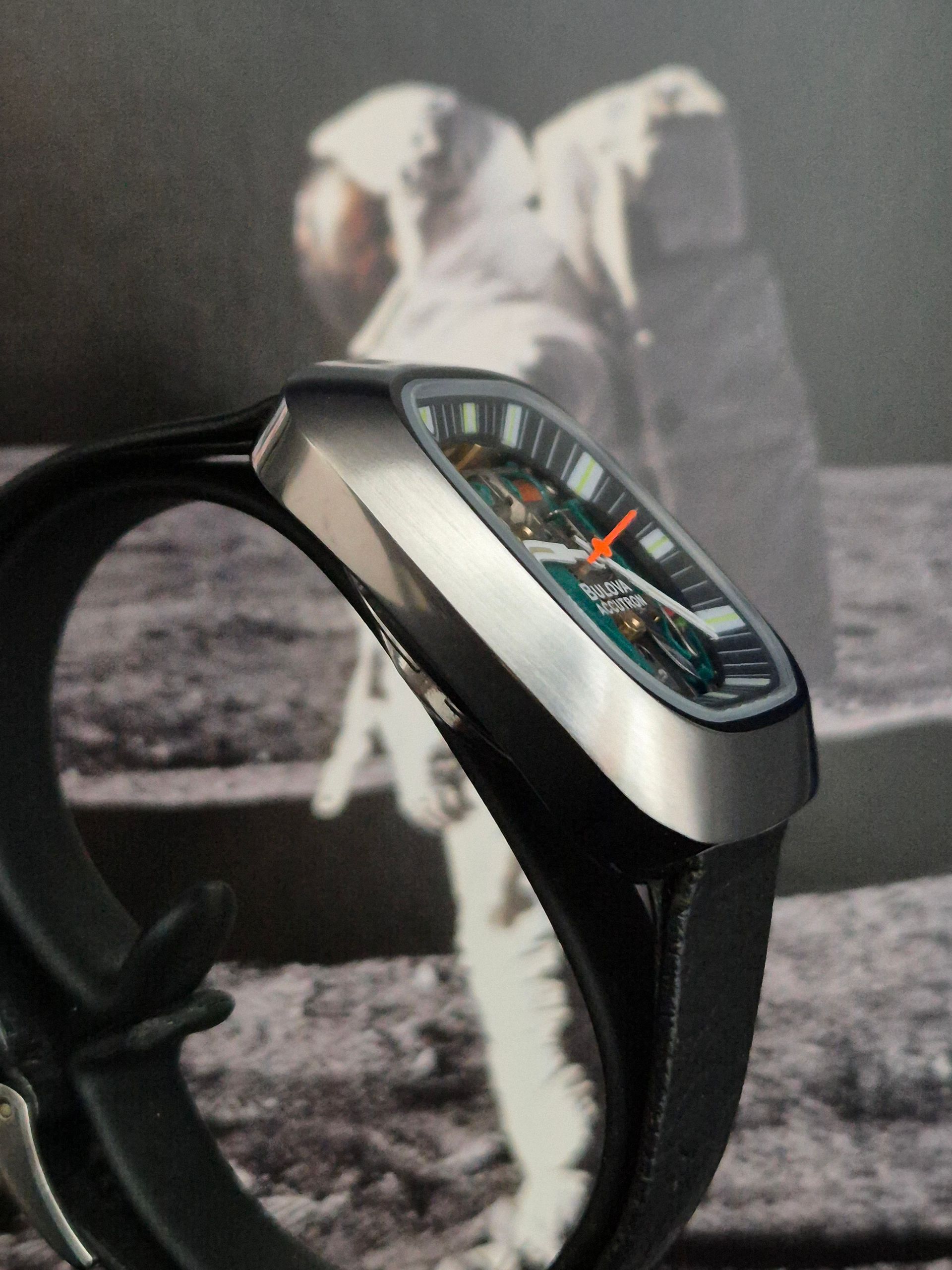 Close-up of a sleek black wristwatch with silver bezel, set against a blurred astronaut image background