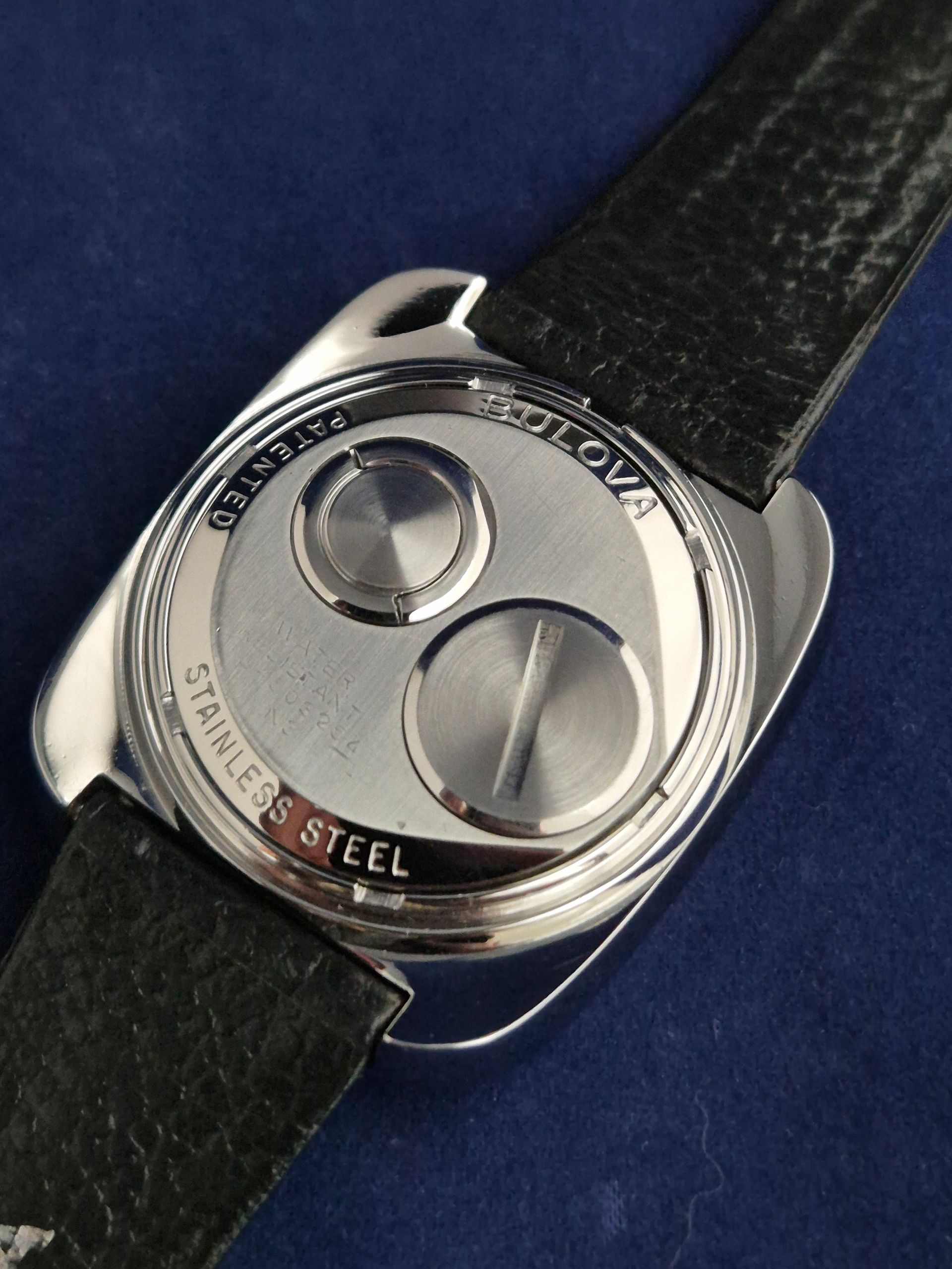 Close-up of a stainless steel watch back with a black leather strap on a dark blue background