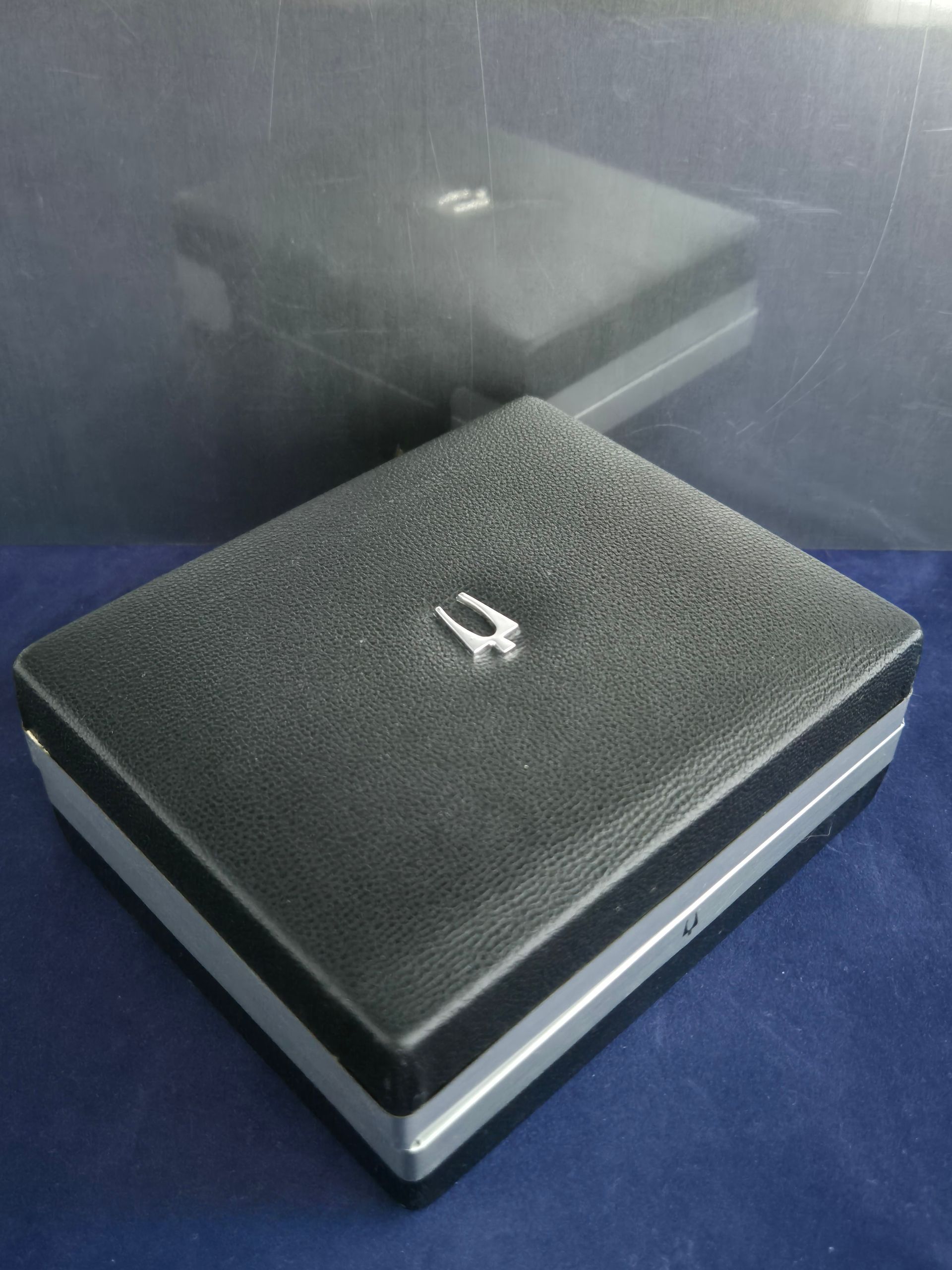 Black textured case with a silver latch on a blue surface, reflected in a mirror behind it
