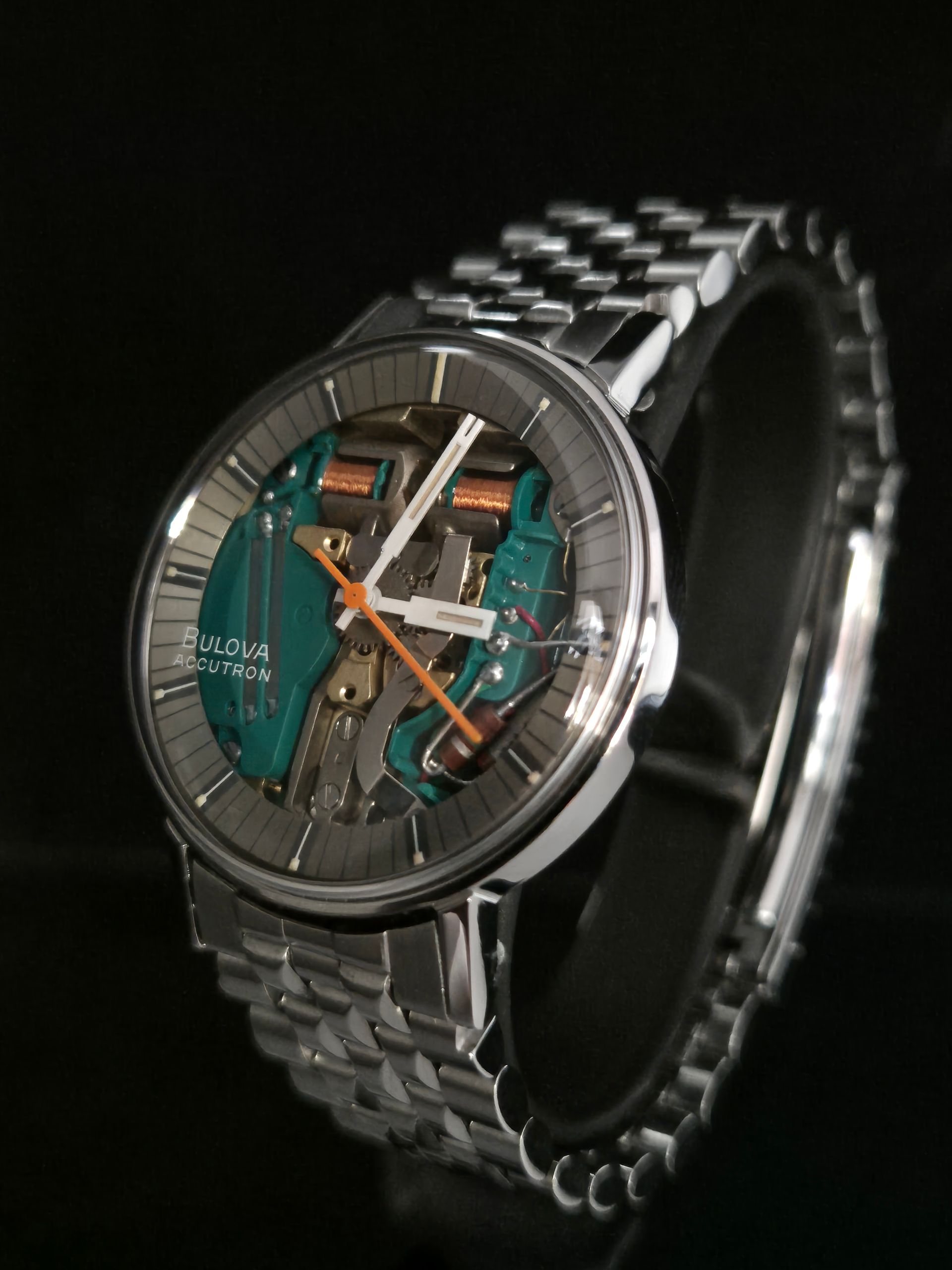 Silver skeleton wristwatch with teal inner components on a black background