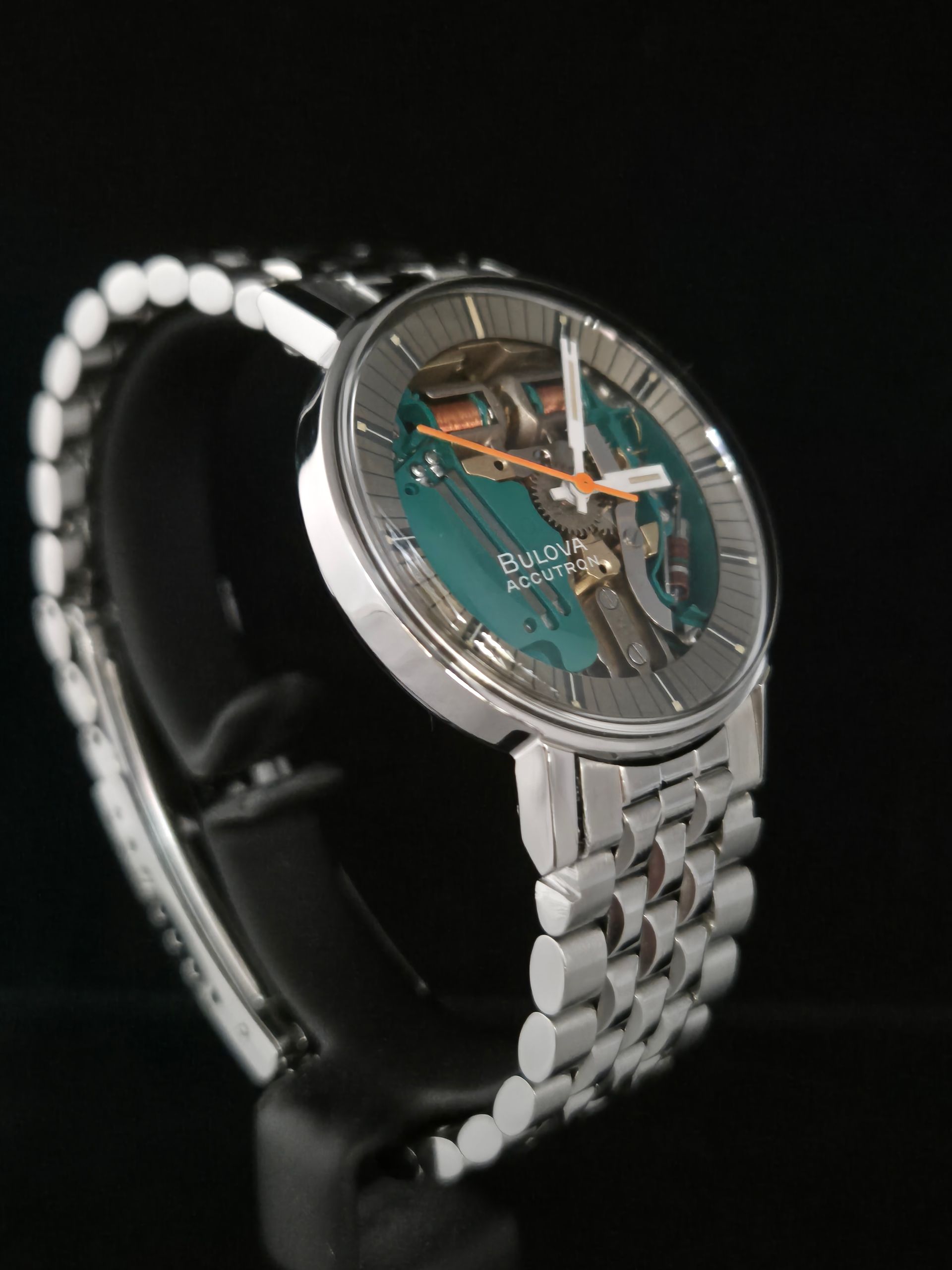 Silver wristwatch with transparent turquoise dial on a black display stand