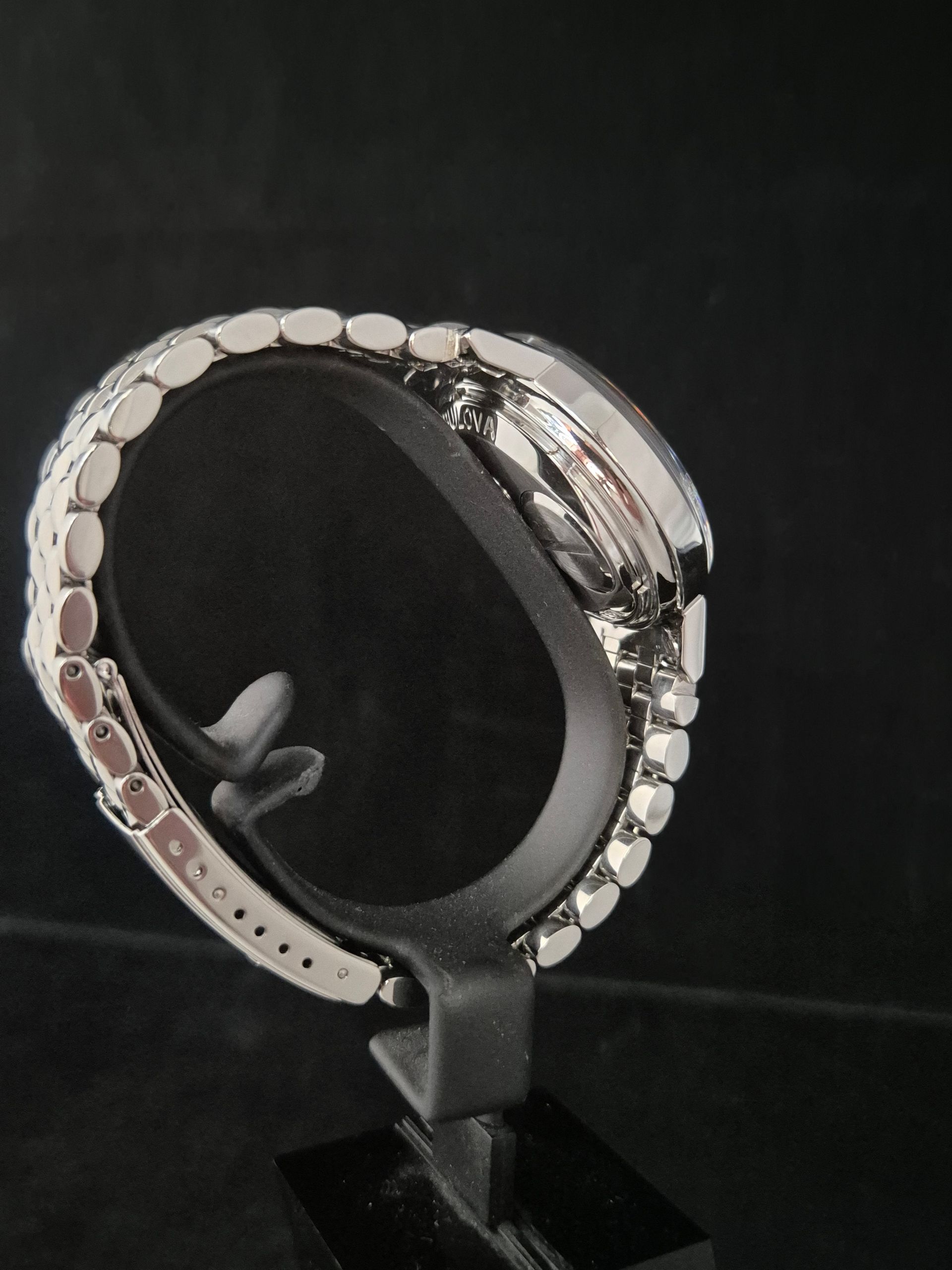Silver wristwatch displayed on a black stand against a dark background.