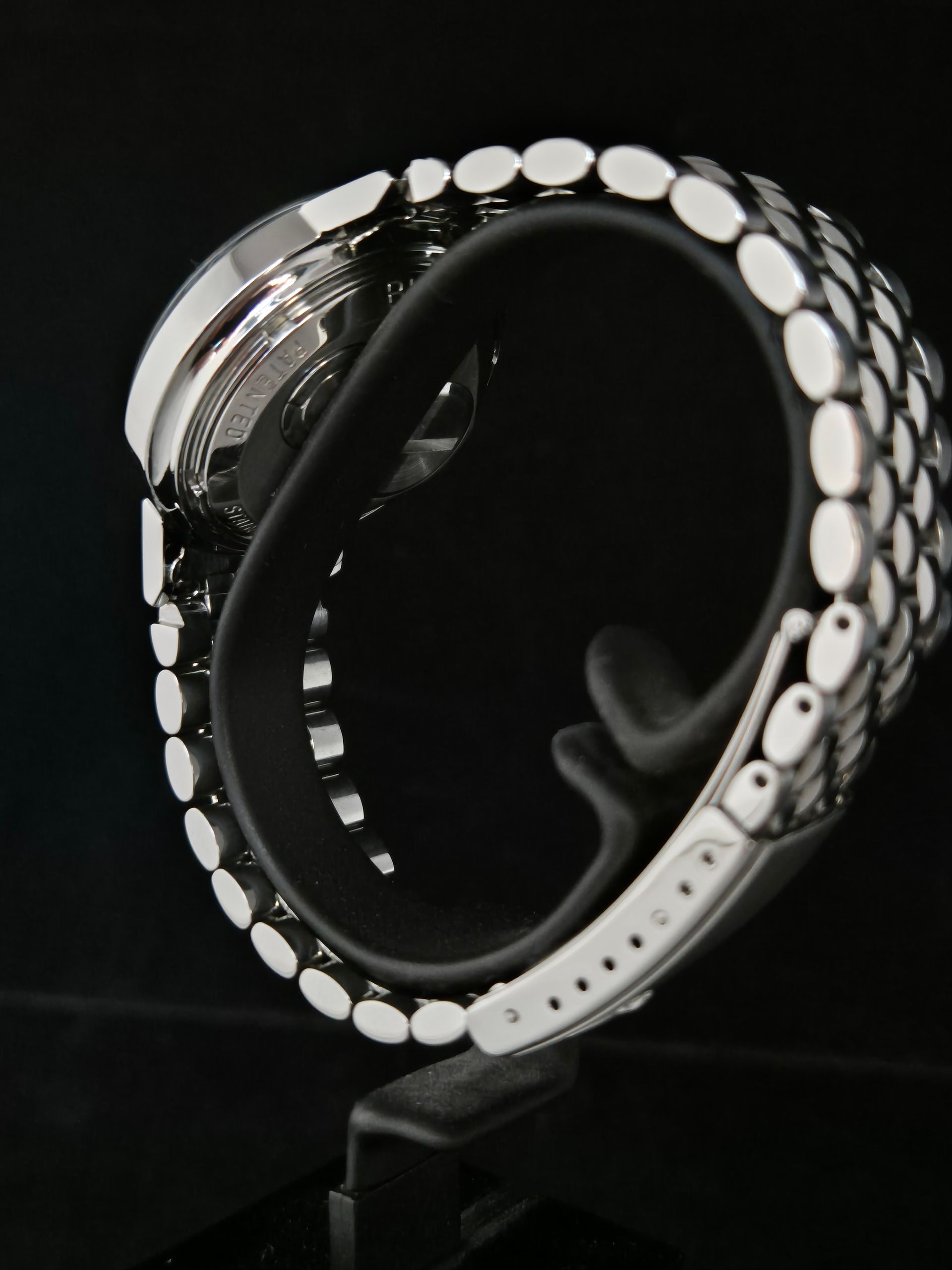 Black smartwatch with a perforated silver band on a display stand.