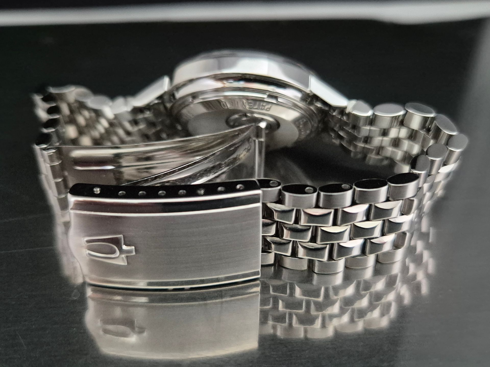 Silver wristwatch with metal band on a reflective surface, close-up view