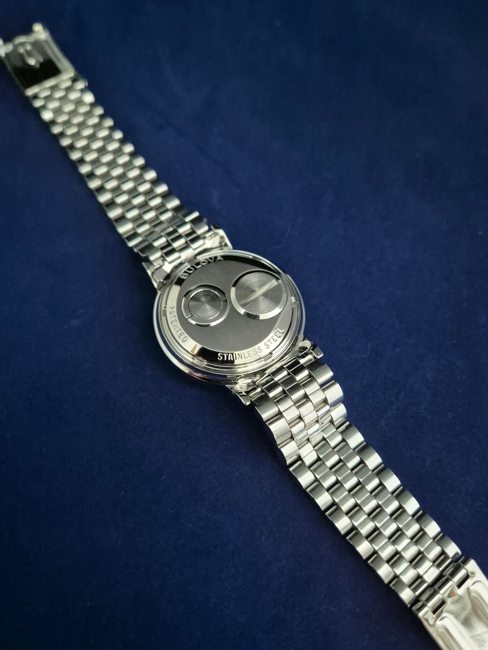 Silver wristwatch with linked bracelet on a dark blue fabric background