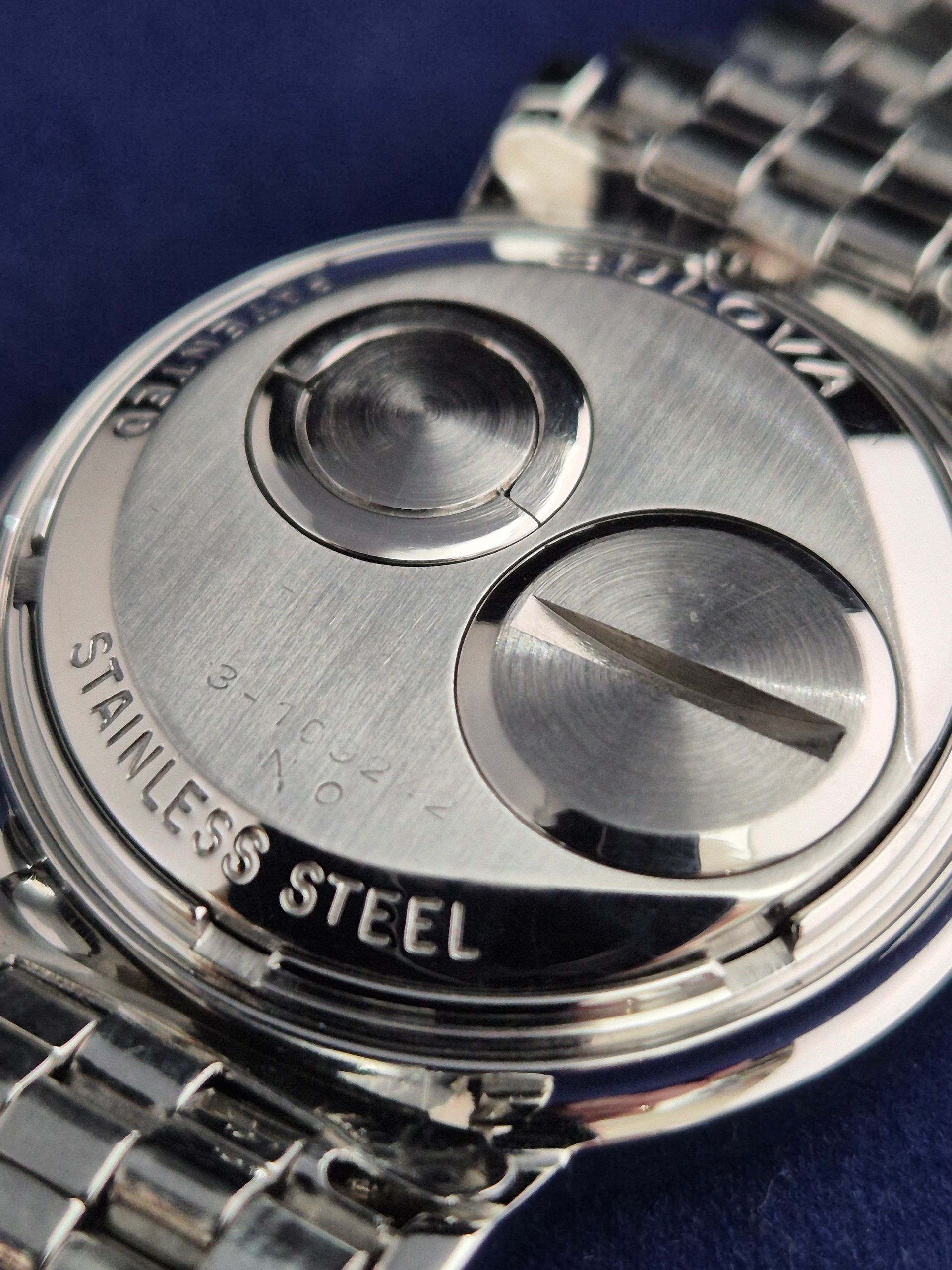 Close-up of a stainless steel watch case back with two buttons and metal bracelet.