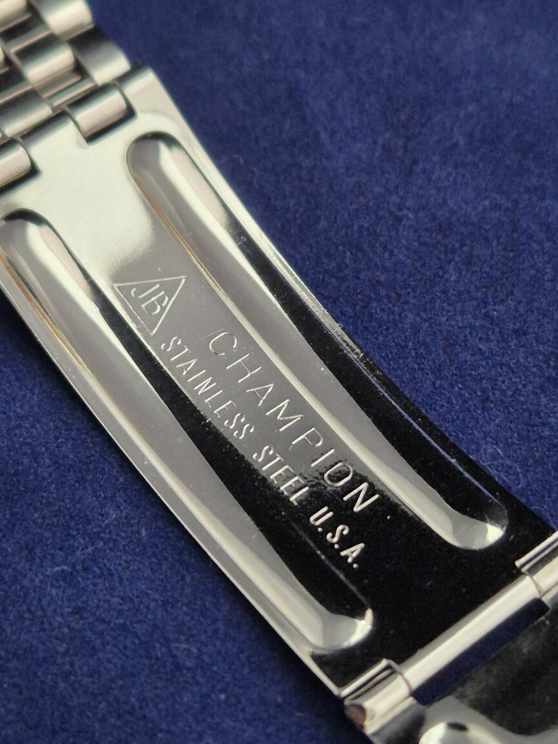 Close-up of a silver metal watch clasp engraved “CHAMPION” on a blue background