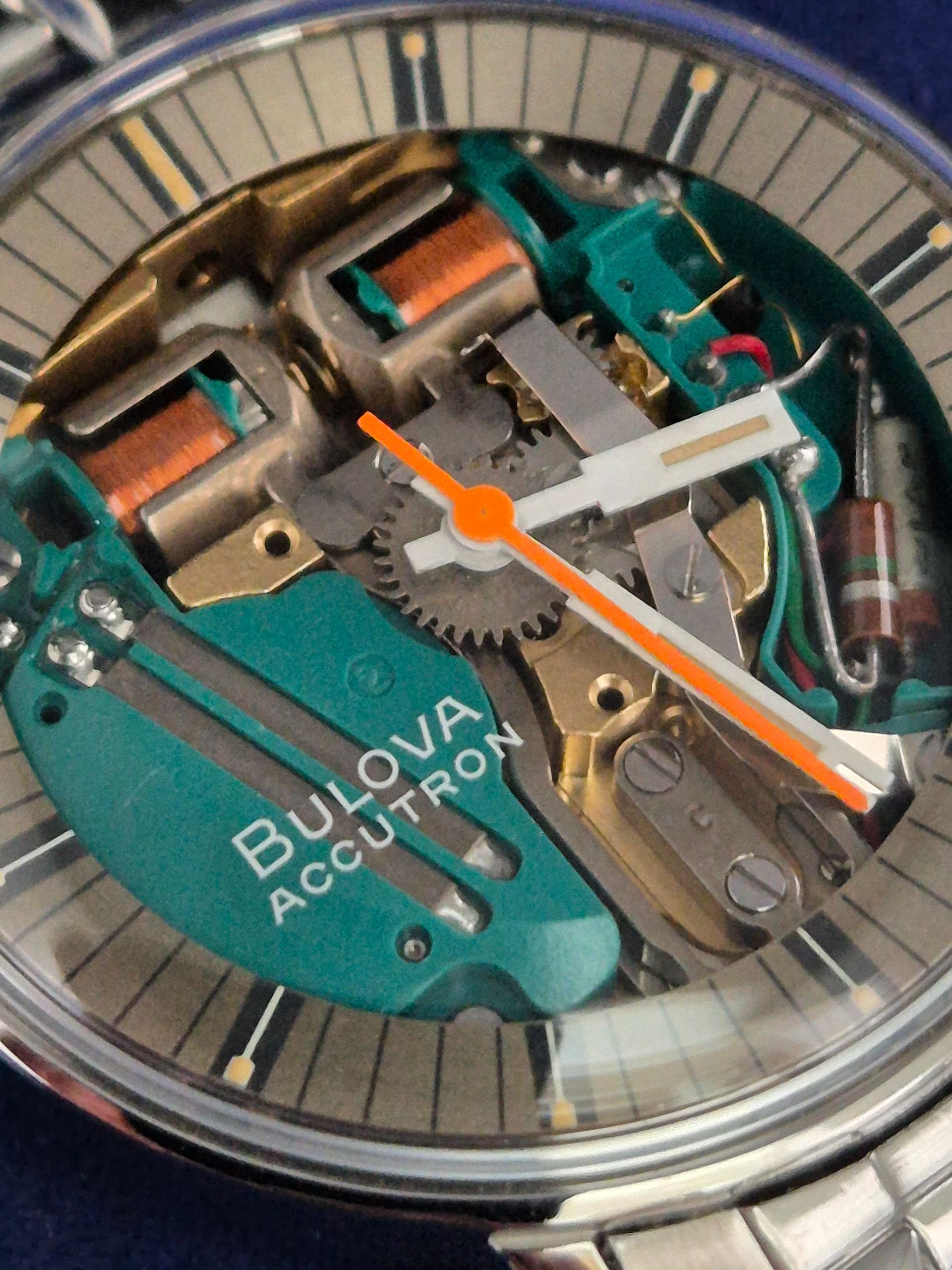 Close-up of a Bulova Accutron watch face with exposed mechanical components and orange hands.