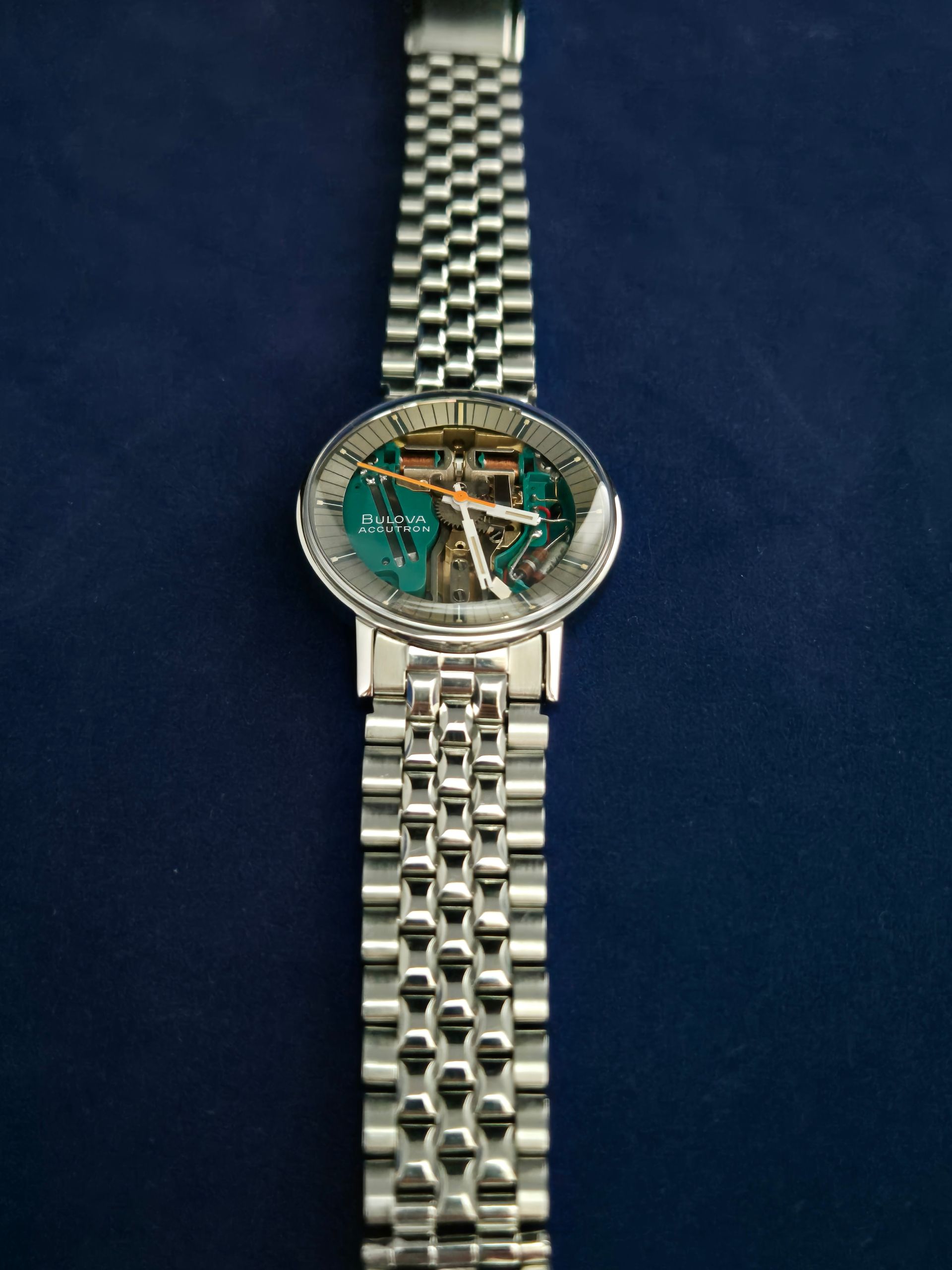 Silver wristwatch with a checkered metal band and green face on a dark blue background