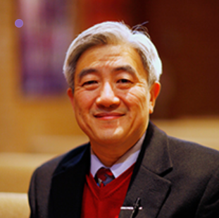 Smiling Asian man in a black suit and red sweater. Silver hair, indoors.