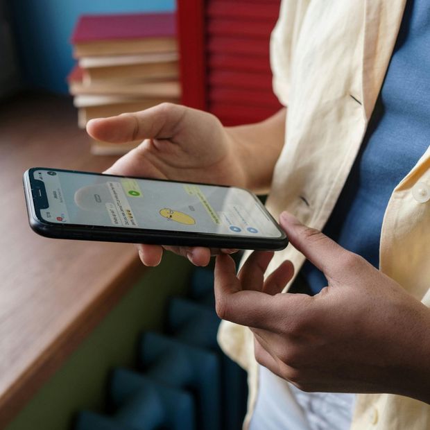 Person holding a phone, messaging. Blue shirt, beige jacket. Phone screen visible.