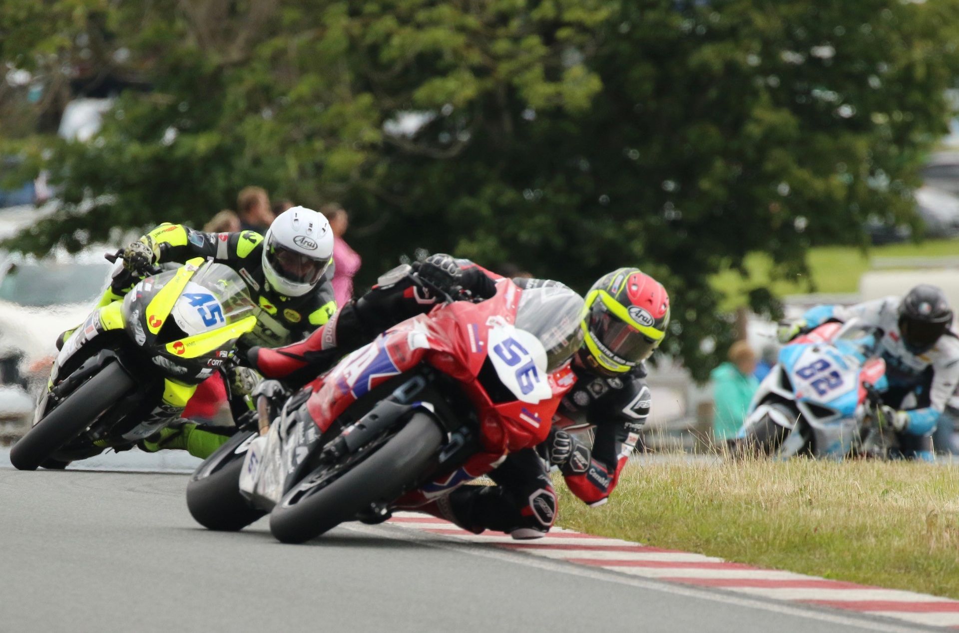 Motorcoureurs leunen in een scherpe bocht op een circuit; de koploper rijdt op een rode motor met nummer 55.