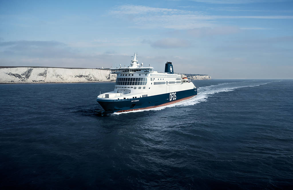 Veerboot op zee, met op de achtergrond witte kliffen en een blauwe lucht.
