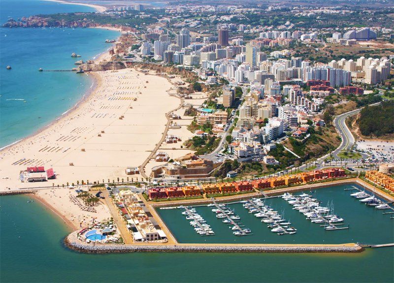 Luchtfoto van Lagos, Portugal, met een zandstrand, een jachthaven met boten en een stadsgezicht van gebouwen langs de kust.