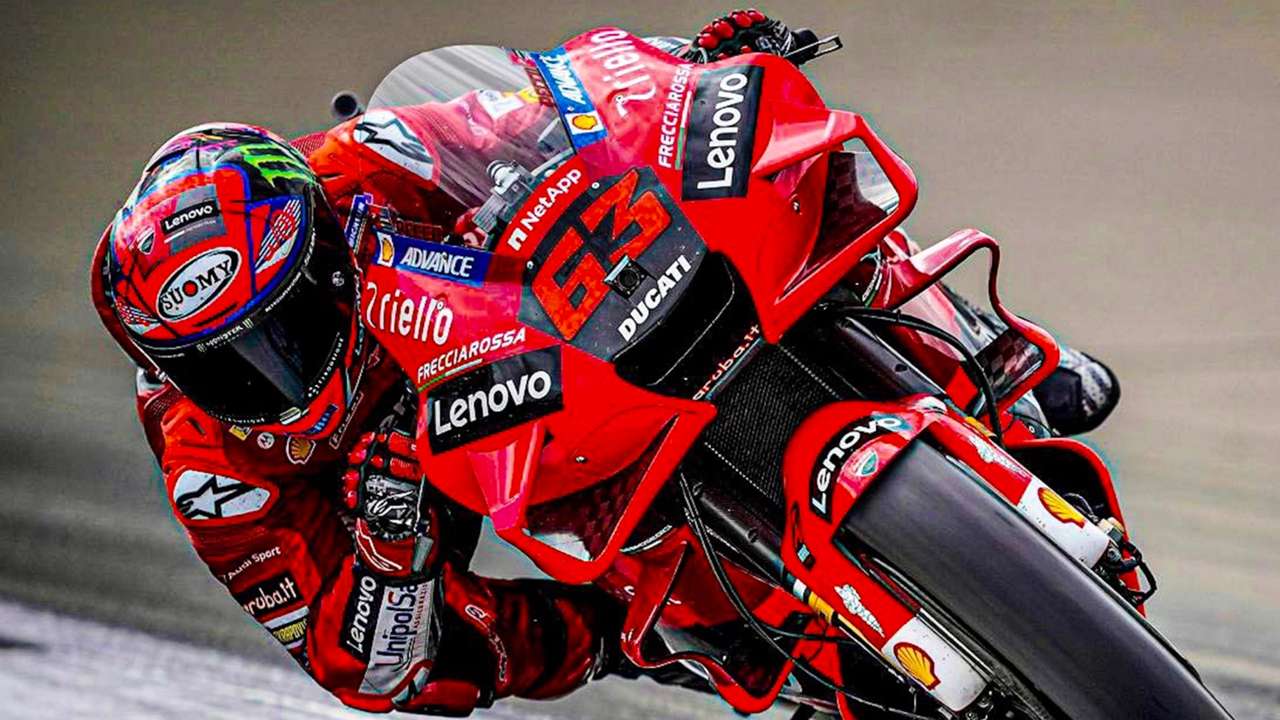Een rode Ducati MotoGP-motorfiets in beweging, bestuurd door een coureur in rode kleding, die schuin de bocht in rijdt.