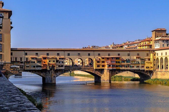 De Ponte Vecchio in Florence, Italië. Een stenen boogbrug met winkels erlangs, over een kalme rivier.