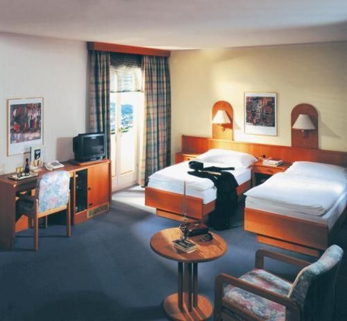 Hotelkamer met twee eenpersoonsbedden, een bureau, een televisie, een kleine ronde tafel met twee fauteuils en een balkon.