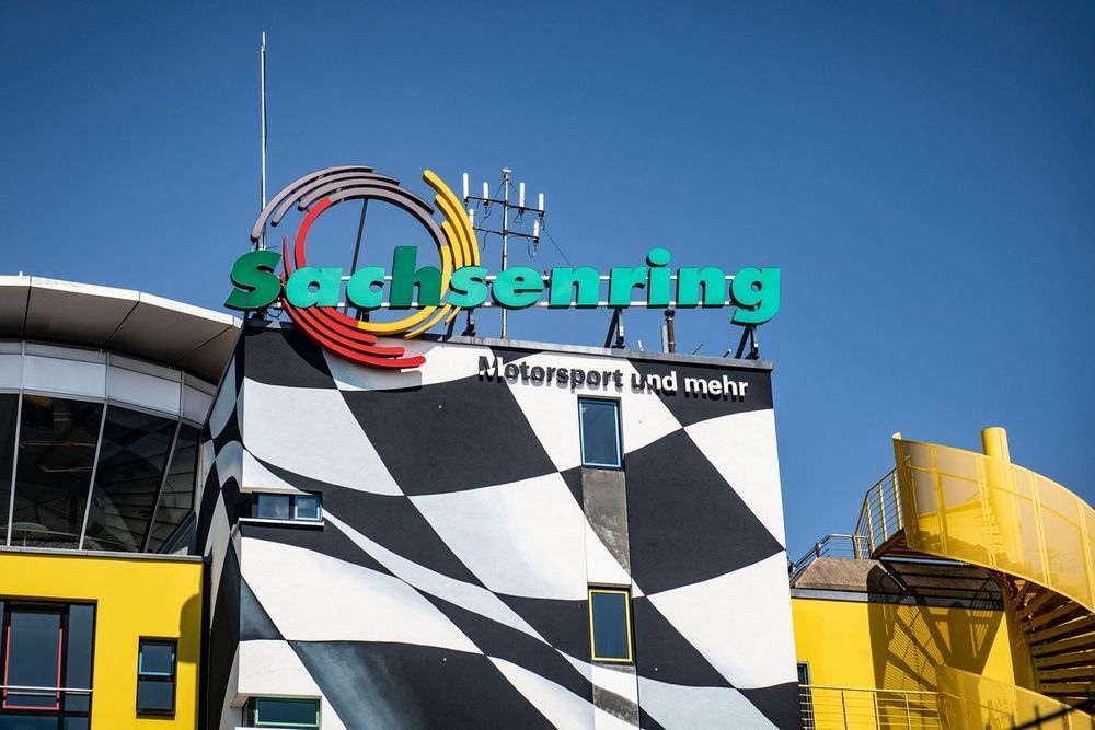 Sachsenring-racebaangebouw met zwart-wit geblokt patroon, groen bord tegen een blauwe lucht.