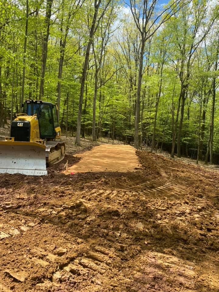 Bulldozer grading a dirt path through a green wooded area on a sunny day