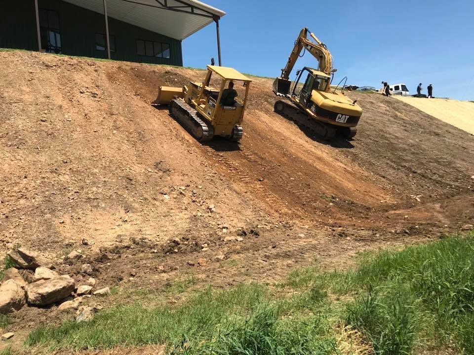 Two excavators working on a steep dirt slope near a building under construction