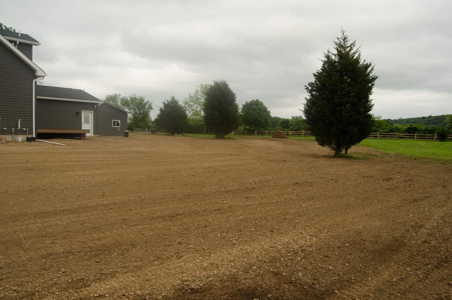 Gravel driveway beside a house and trees under a cloudy sky