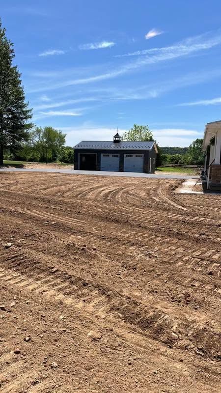 Rural dirt lot with a blue garage, trees, and a clear blue sky