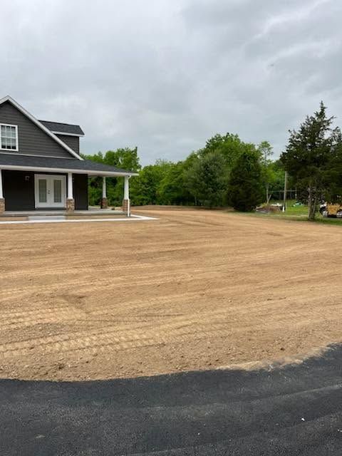 Gravel driveway beside a gray house with a covered porch under cloudy skies.