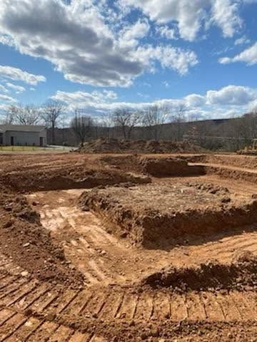 Excavated dirt lot with terraced earth and tire tracks under a partly cloudy sky