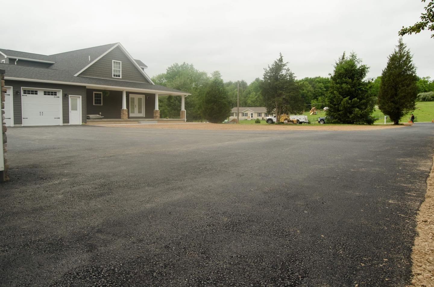 Large empty gravel driveway beside a house and garage under a cloudy sky