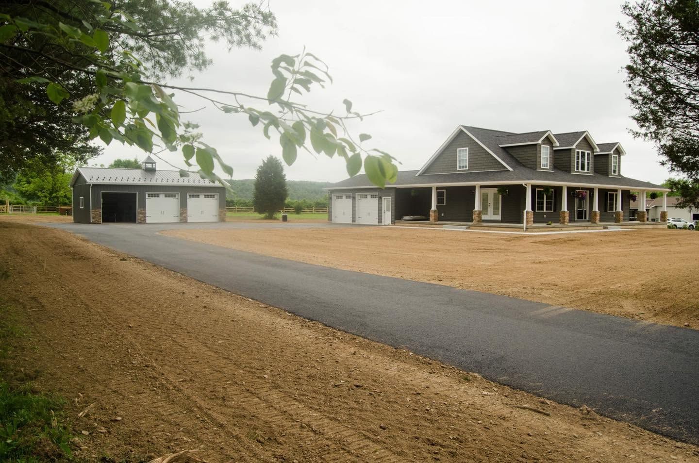 Rural driveway leading to a large house and two detached garages on a foggy, overcast day
