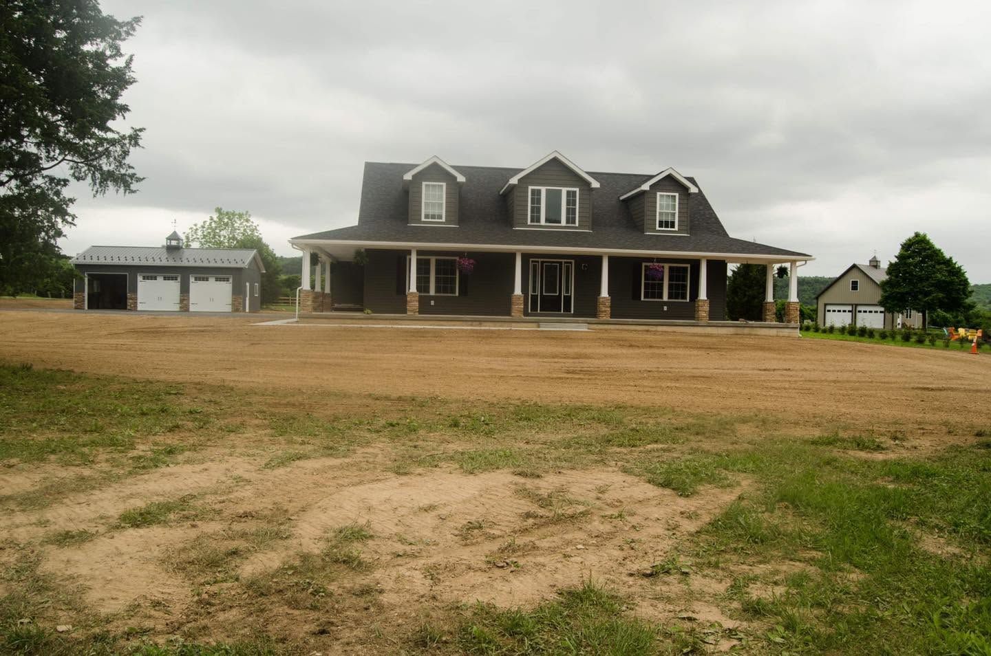 Large two-story house with a front porch and detached garage on a cloudy rural lot