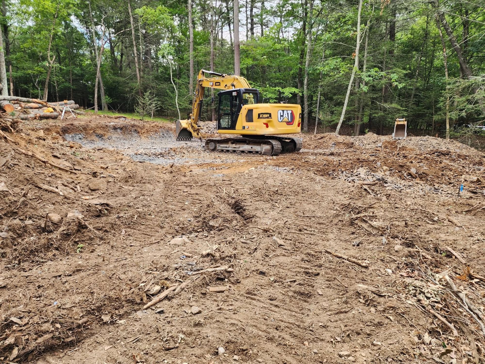 Yellow excavator on a muddy construction site surrounded by trees