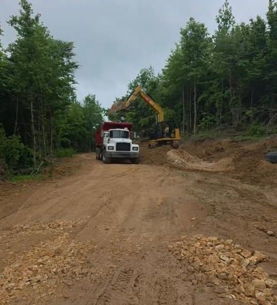 Dump truck and excavator working on a dirt road in a wooded area