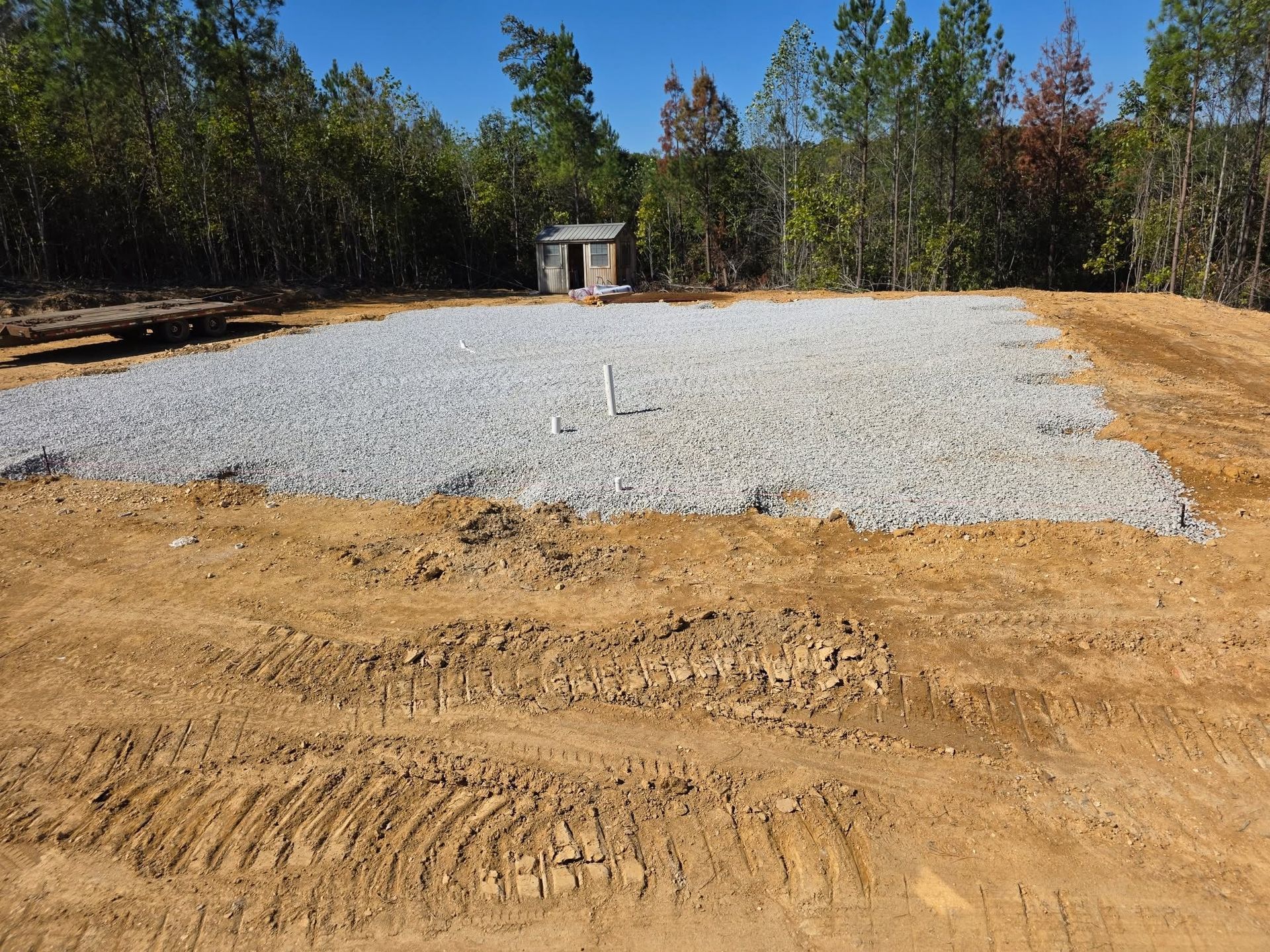 Gravel pad in a wooded clearing with a small shed in the distance and dirt foreground