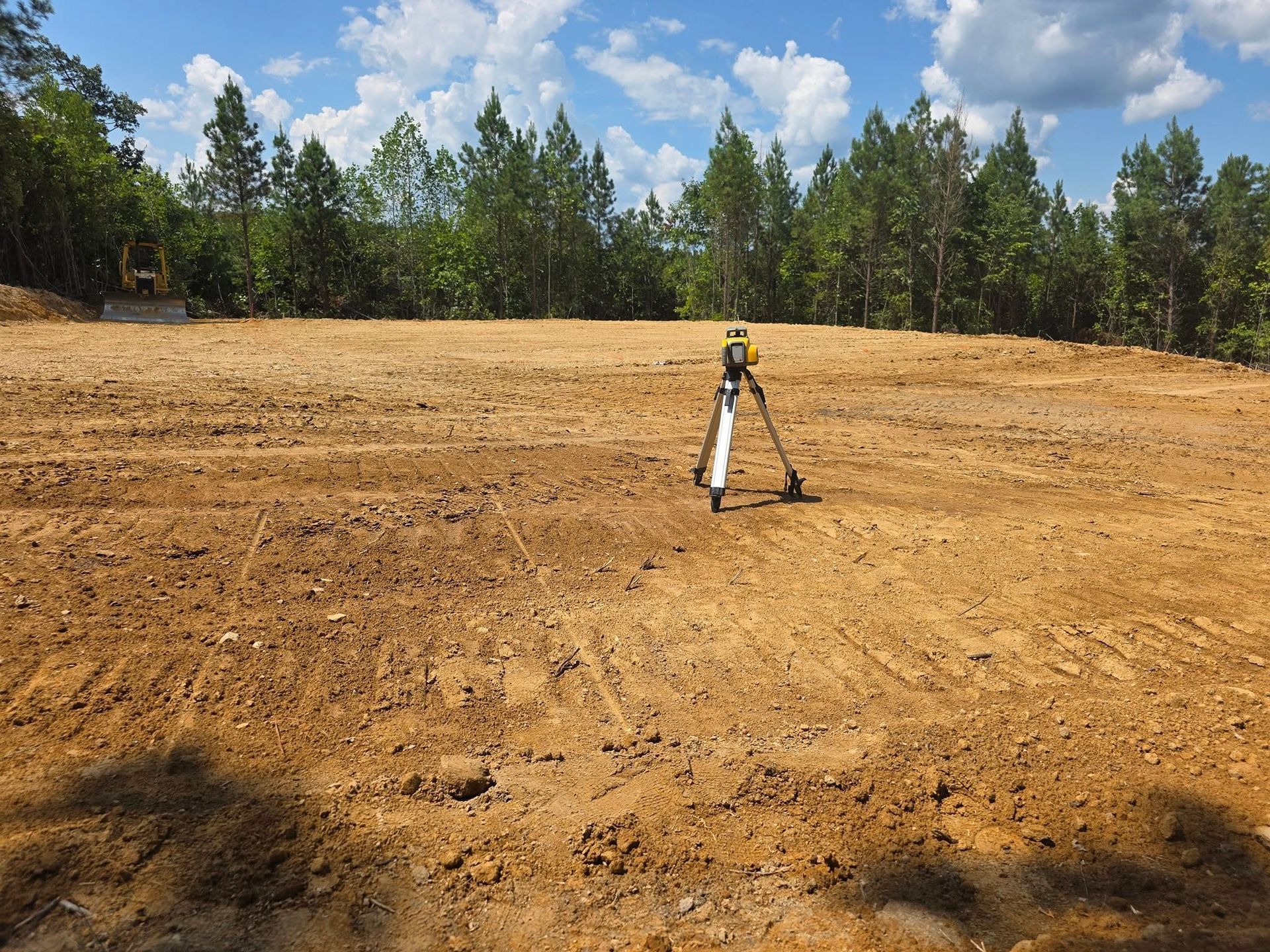 Surveying equipment on a cleared dirt field with trees and blue sky in the background